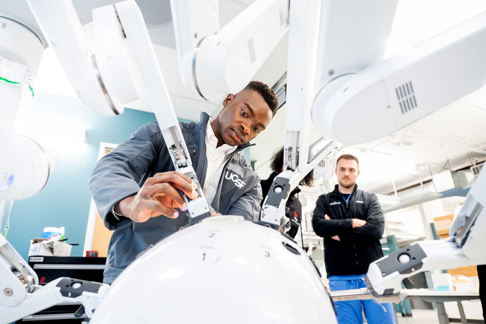 An intern works with the arms of a surgical robot with instructors watching on.