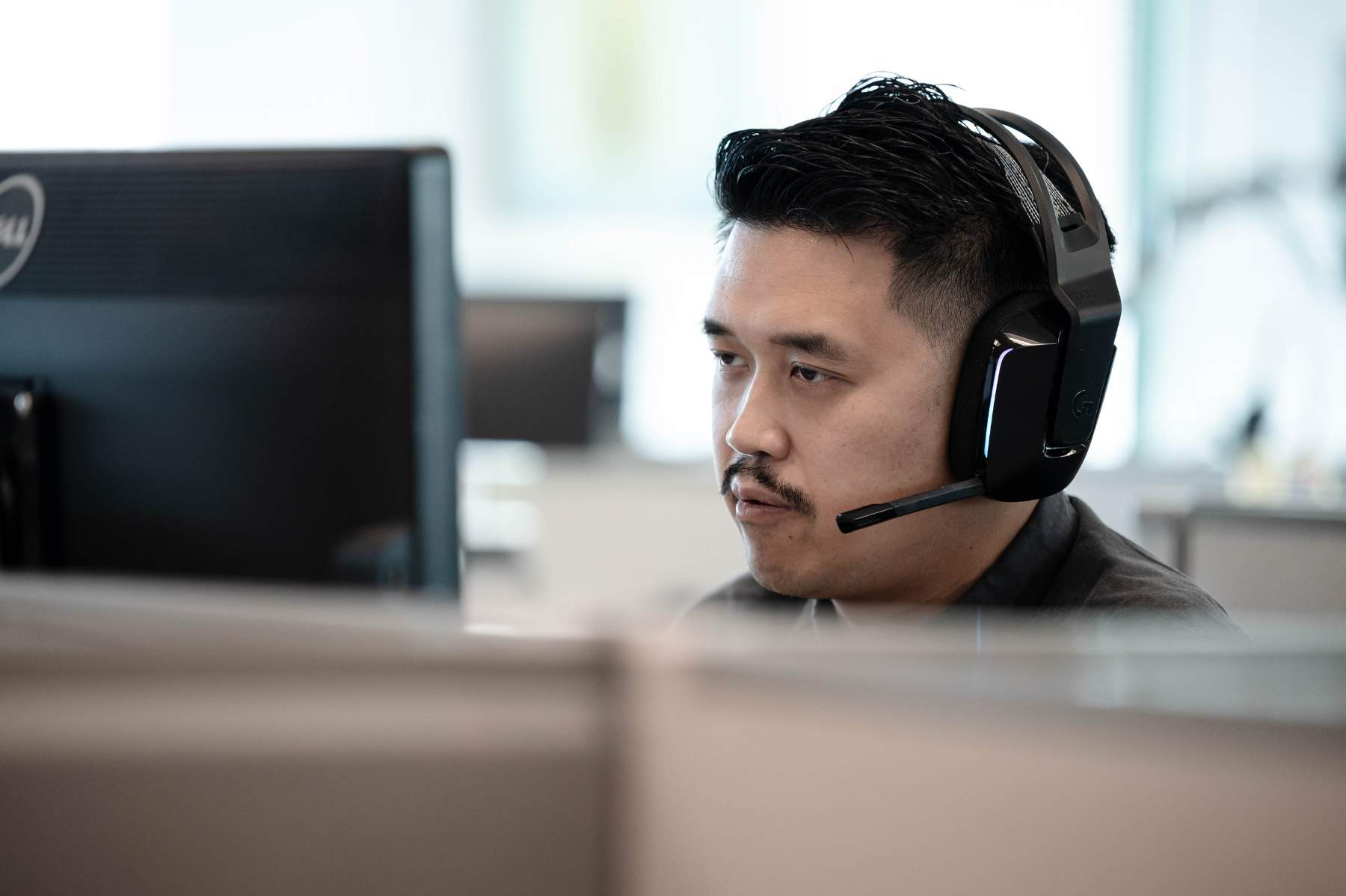  A man wearing a headset, intently focused on his computer monitor.