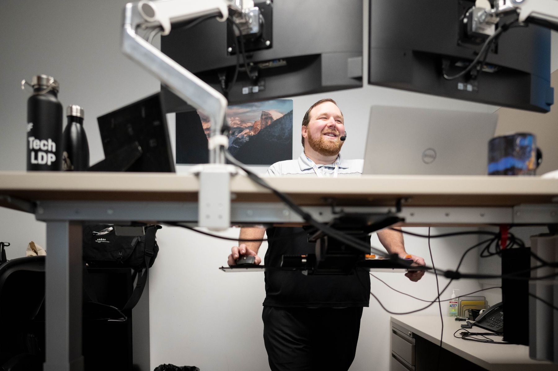 A man smiling while standing at a height-adjustable desk.