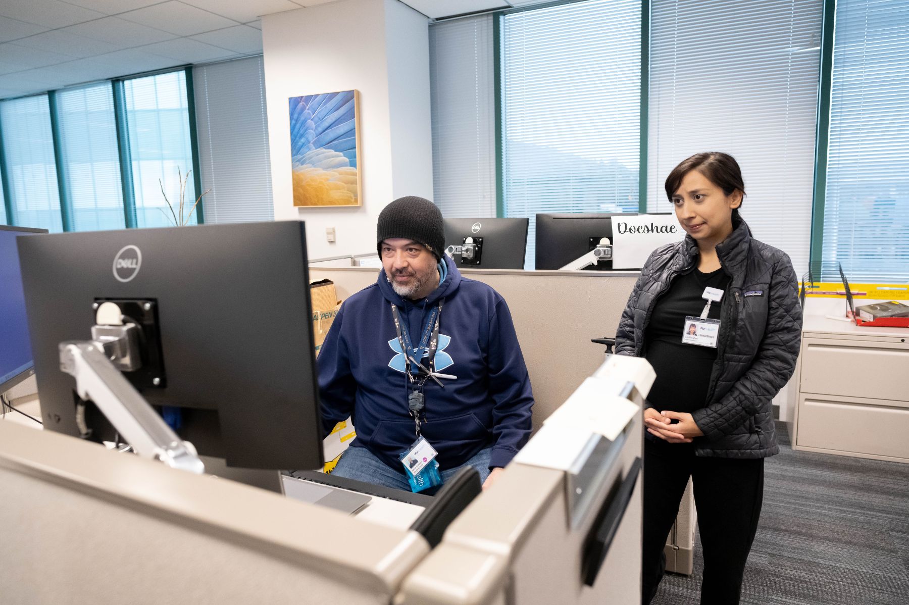 Two IT professionals, a man and a woman, looking at a computer monitor at a workstation.