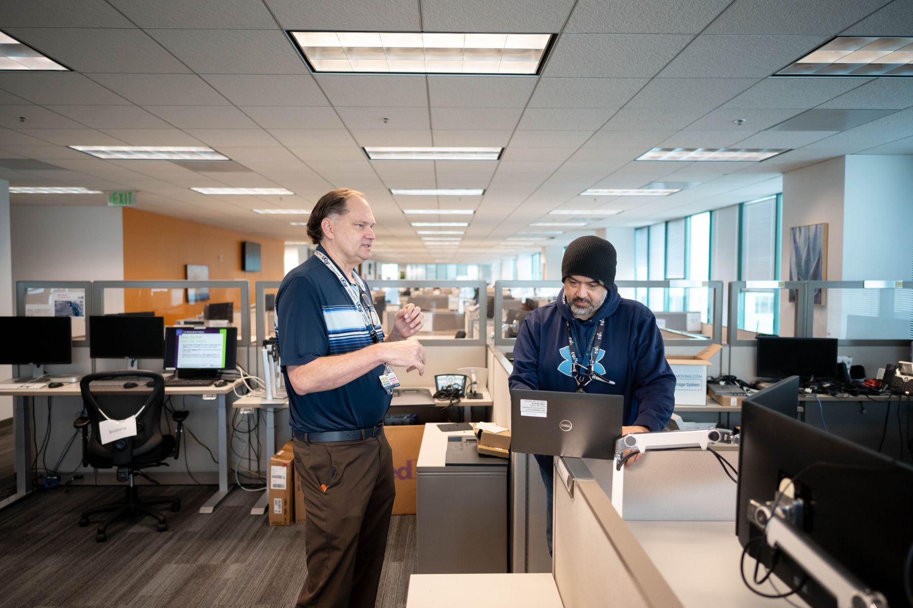 Two men in an office cubicle area, standing and talking.