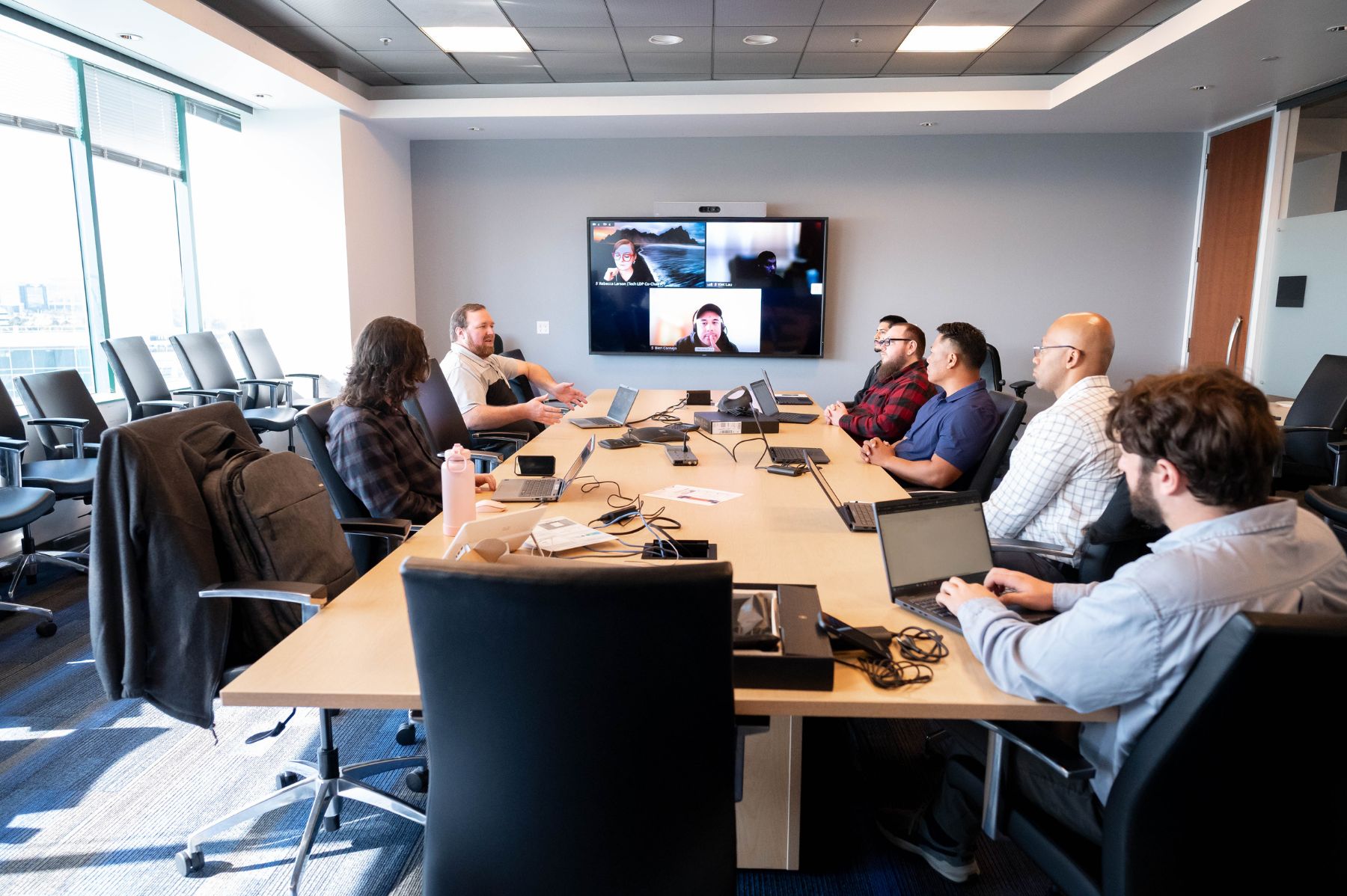 A group of people at a conference table collaborating in a hybrid meeting.