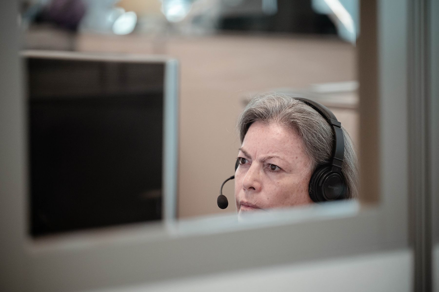 A woman wearing a headset, looking at a computer monitor.