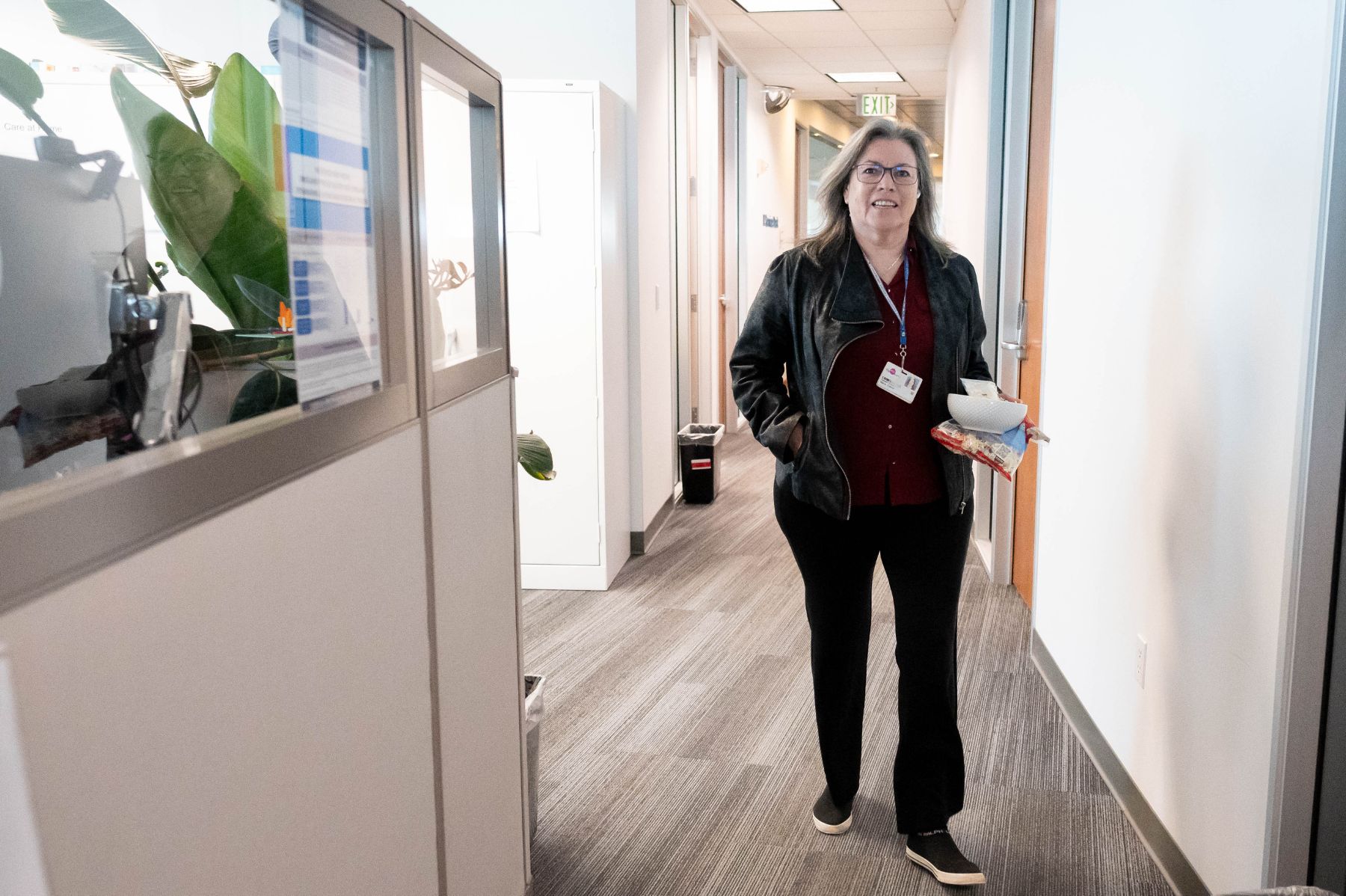 A woman smiling while walking down a hallway, carrying a lunch container.