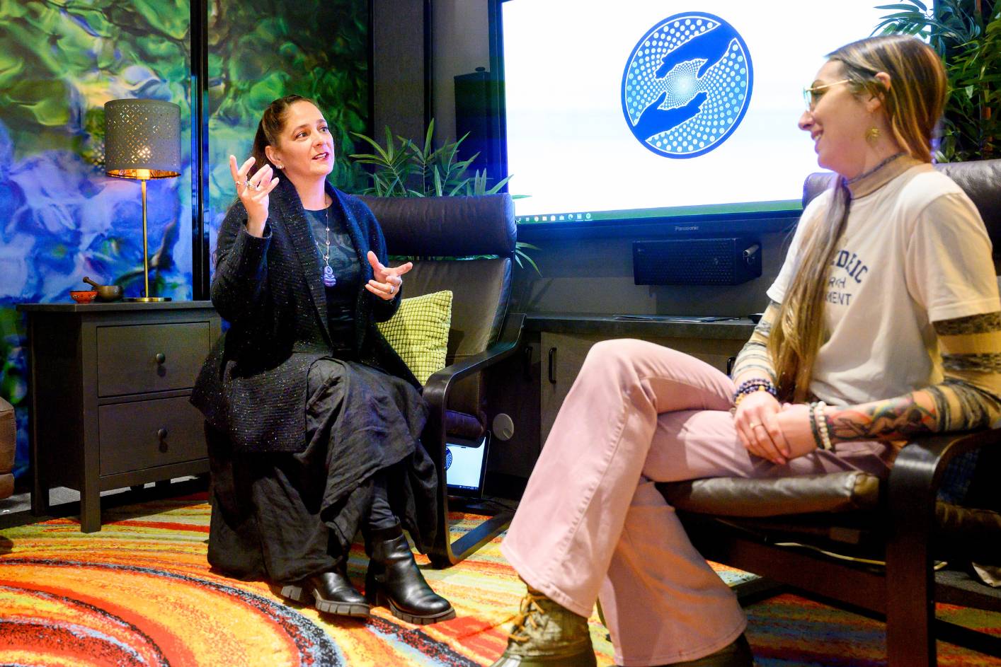 PI Jennifer Mitchell sits in chair connecting with colleague in colorful room.
