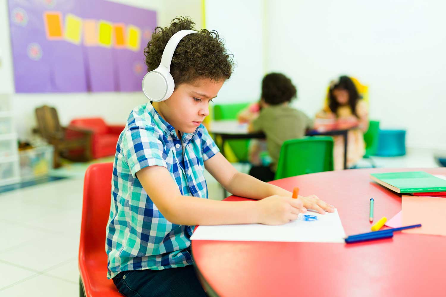 A young boy wears headphones inside a kindergarten classroom.