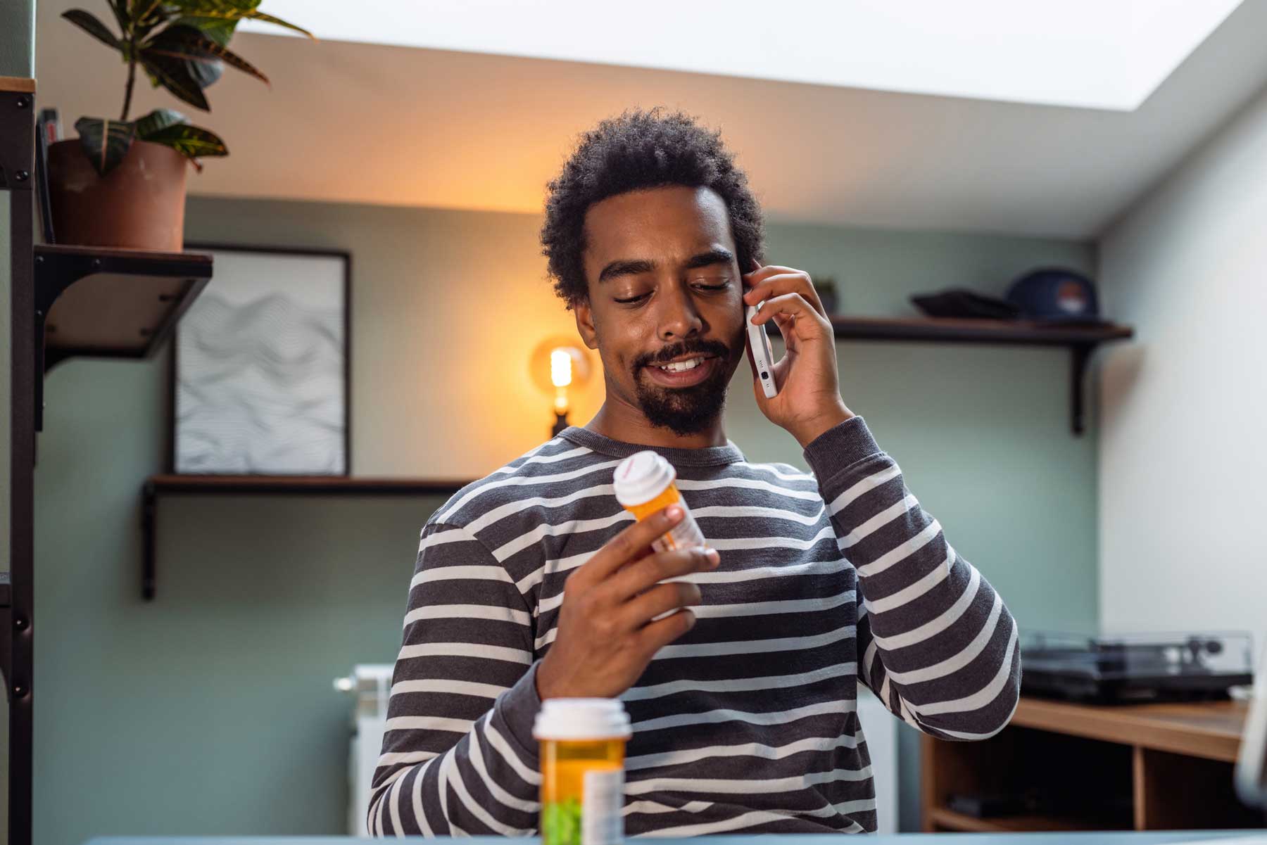 A young Black man receives telehealth care as he looks at his medications.
