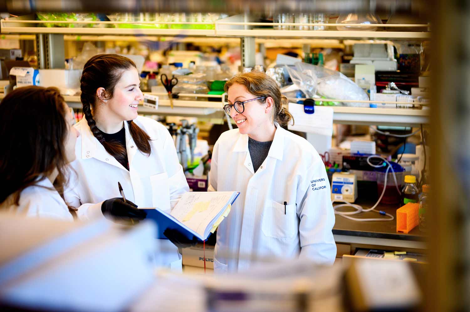 Balyn Zaro and graduate students wear white lab coats as they discuss in Dr. Zaro's lab.