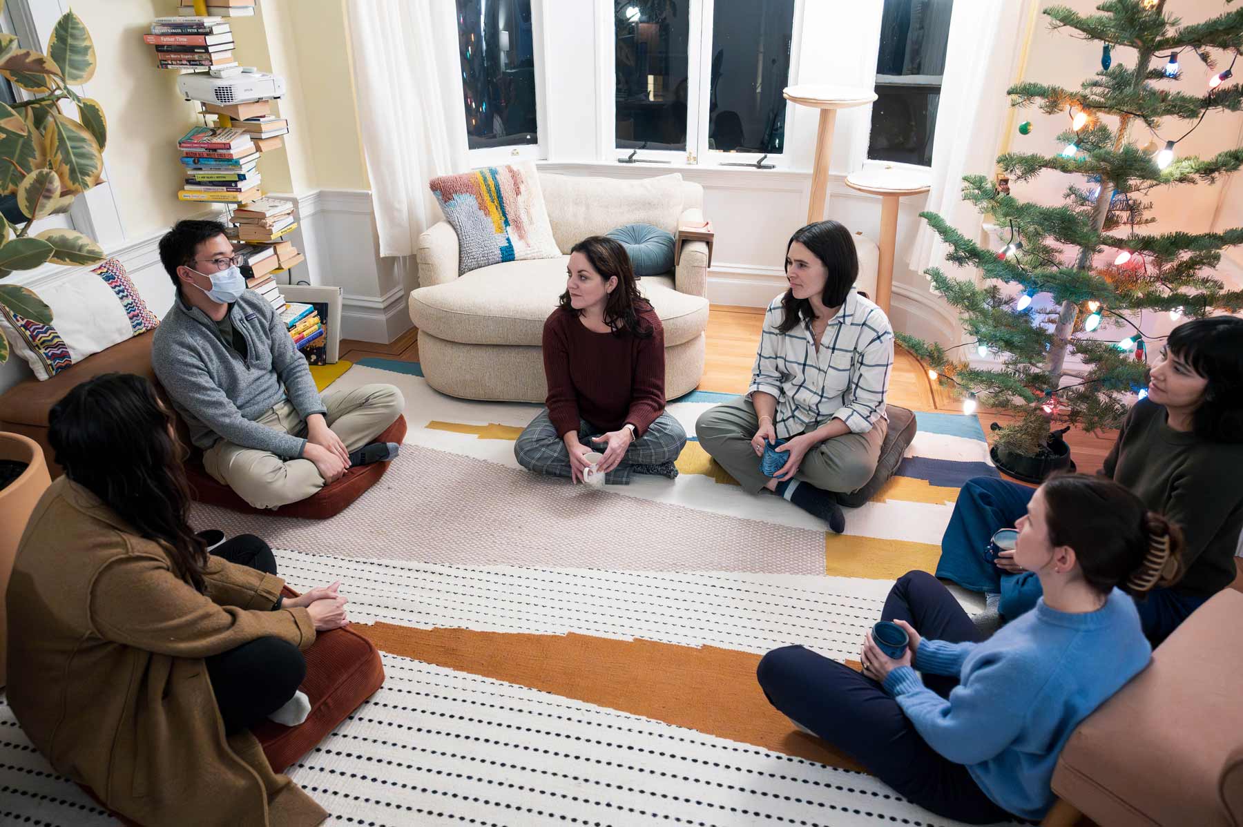 Larissa Thomas sits in a circle with residents for a group meeting inside a cozy living room area.