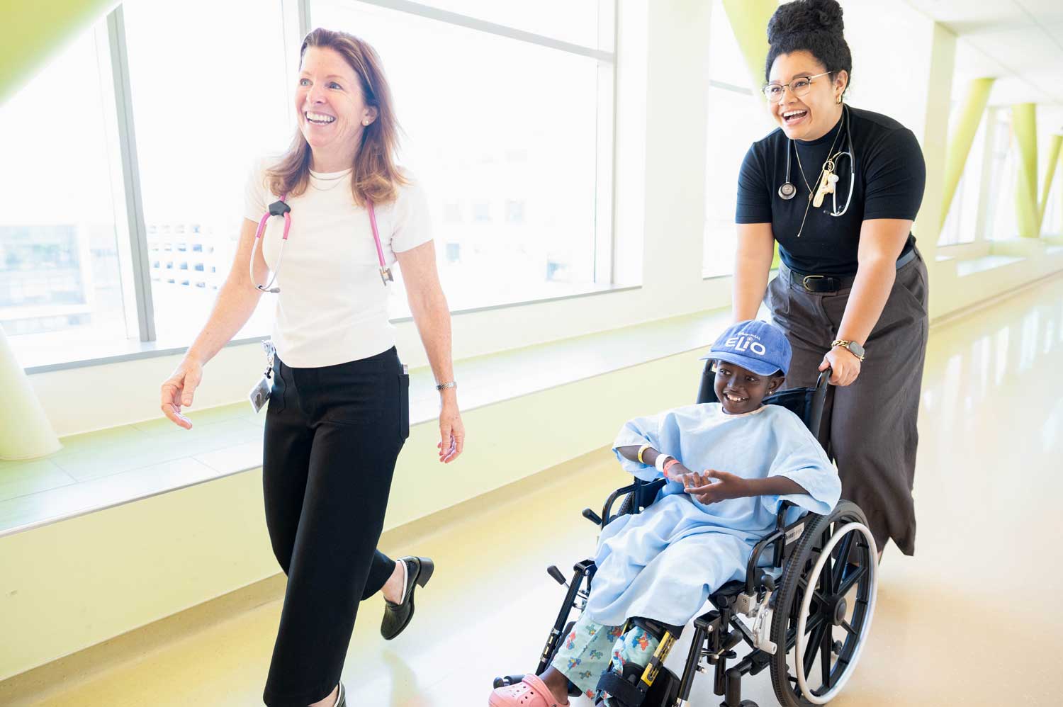 Michele Long walks with Kathleen Wallace as she pushes a pediatric patient from Tanzania along in a wheelchair.