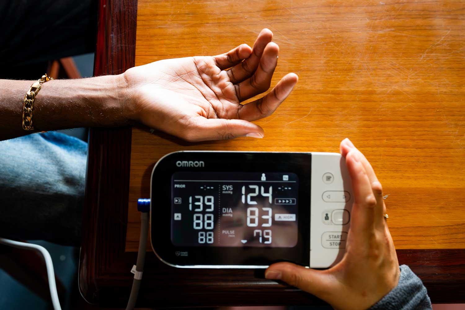 A close-up shot of a person's arm extended as a health practitioner measures their blood pressure with an at-home blood pressure monitor.