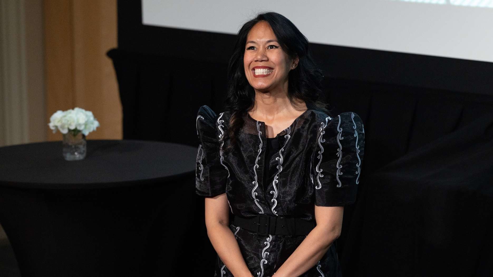 Dr. Jennifer Cocohoba stands on stage on stage smiling proudly.