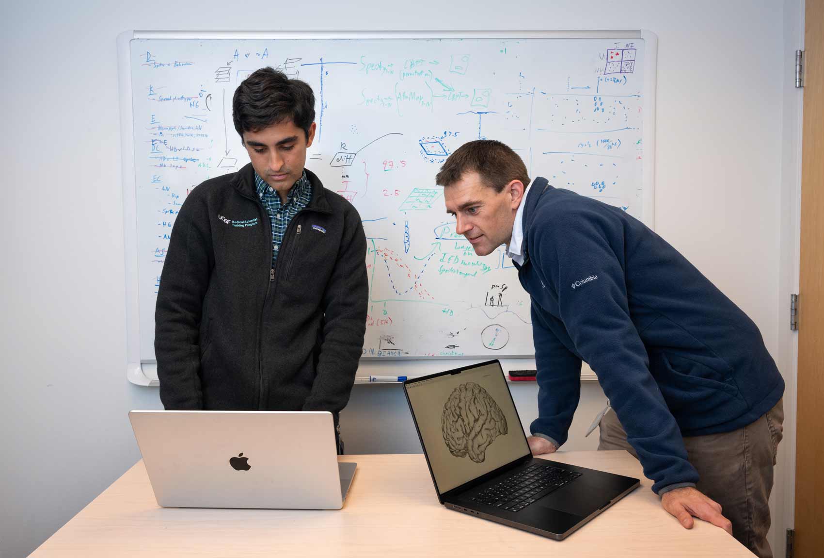 Researchers Alex Silva and Jon Kleen work at a whiteboard while looking at data on a computer screen.