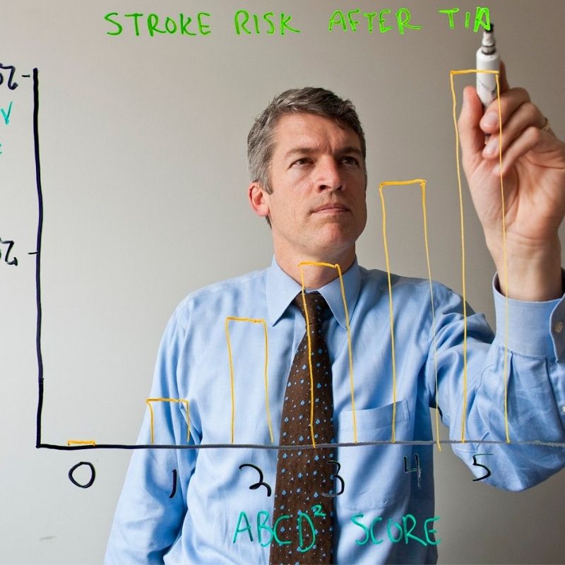 Clay Johnston stands at a board drawing a graph showing the rise of stroke incidents.