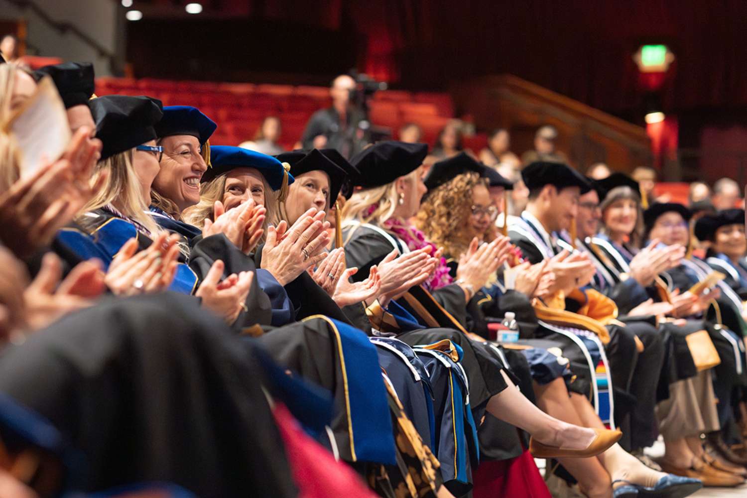 Long row of graduates in regalia applaud.