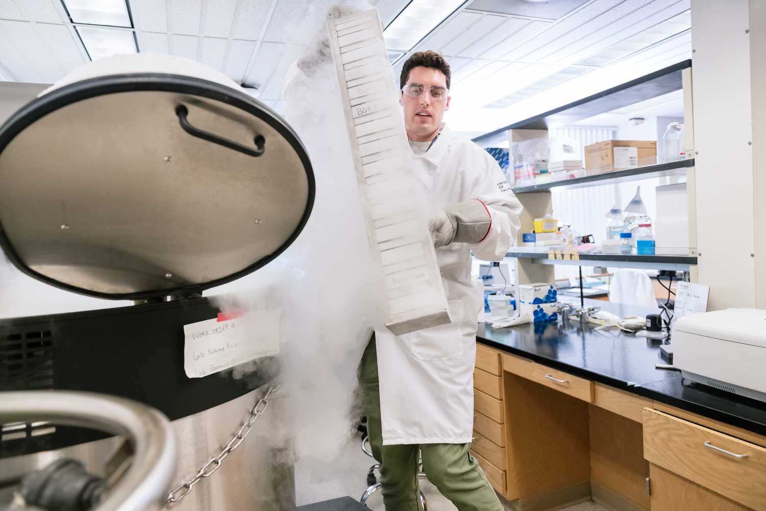 A lab worker in a white lab coat pulls out frozen samples from a nitrogen tank in a lab.