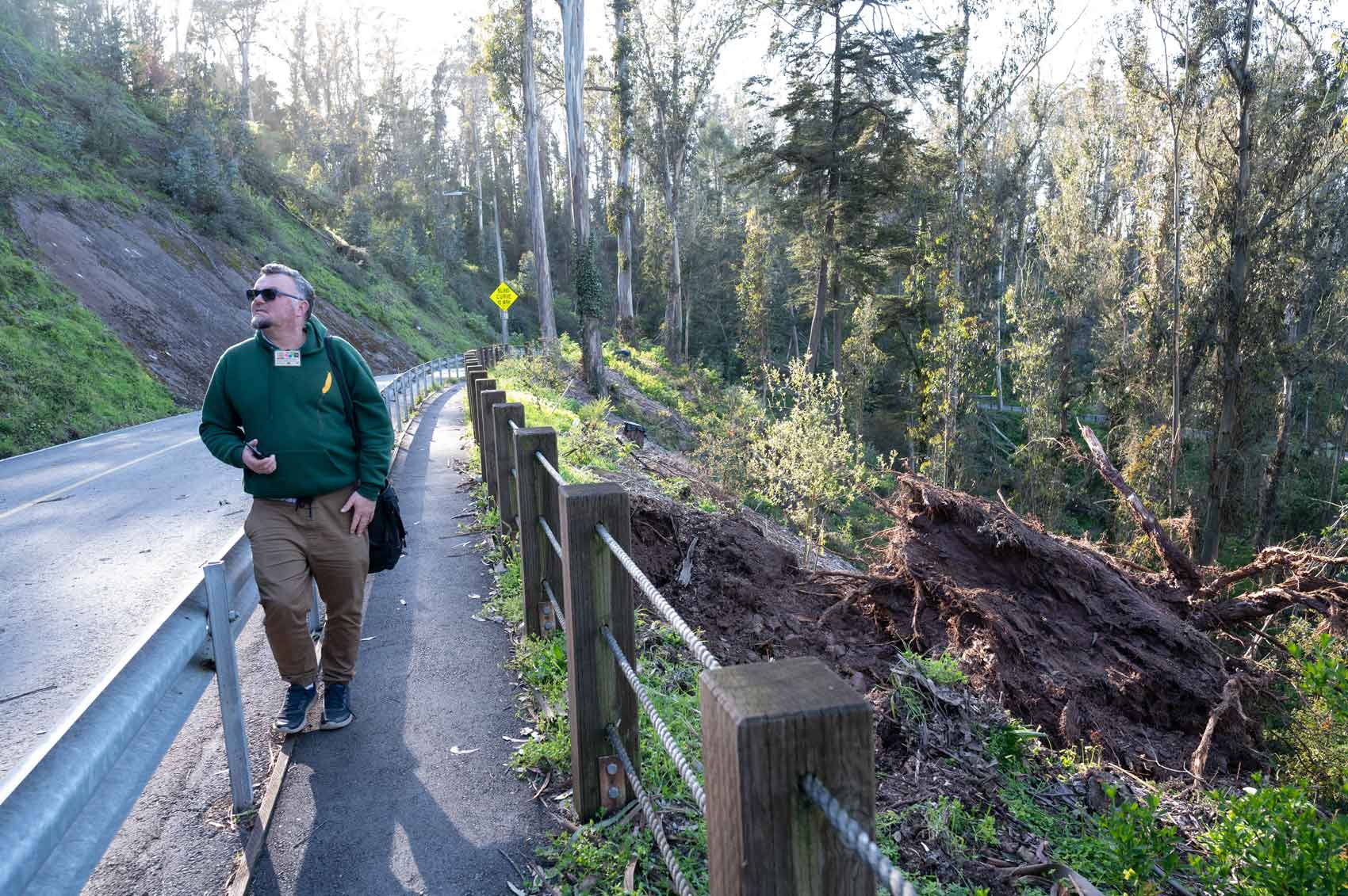 A man walks on a sidewalk at Mount Sutro, surrounded by trees and lush greenery.