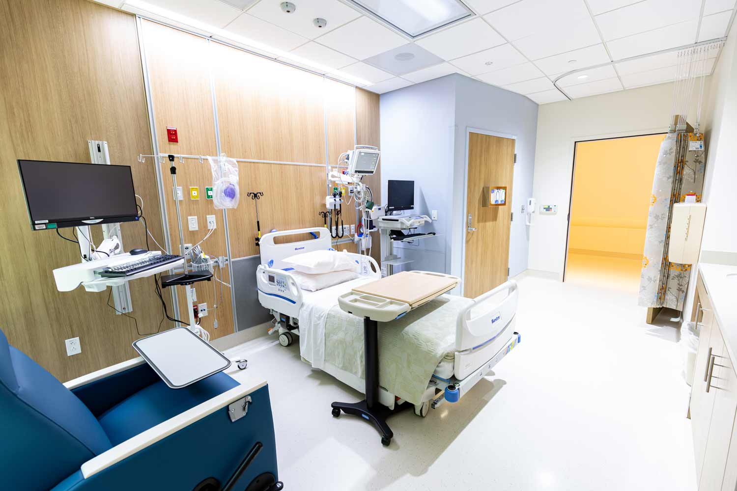 A hospital room with a hostpial bed, lounging chair, and array of medical equipment.