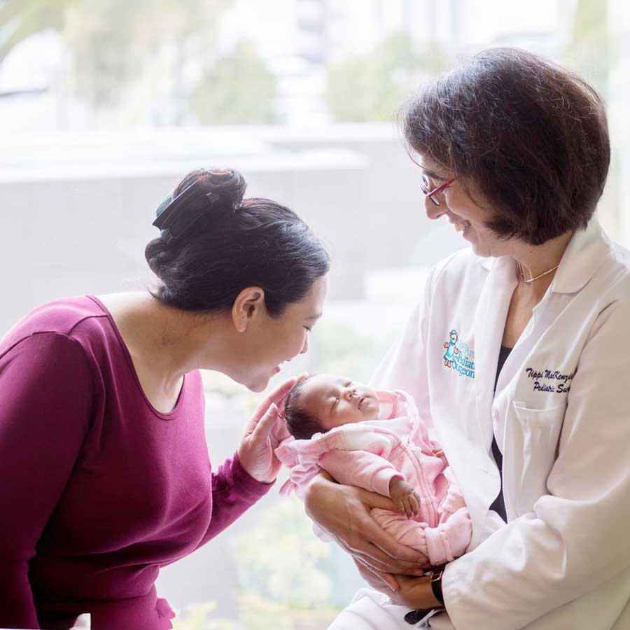 Neonatal surgeon Tippi Mackenzie holds a newborn baby as her mother smiles and holds the baby's head.