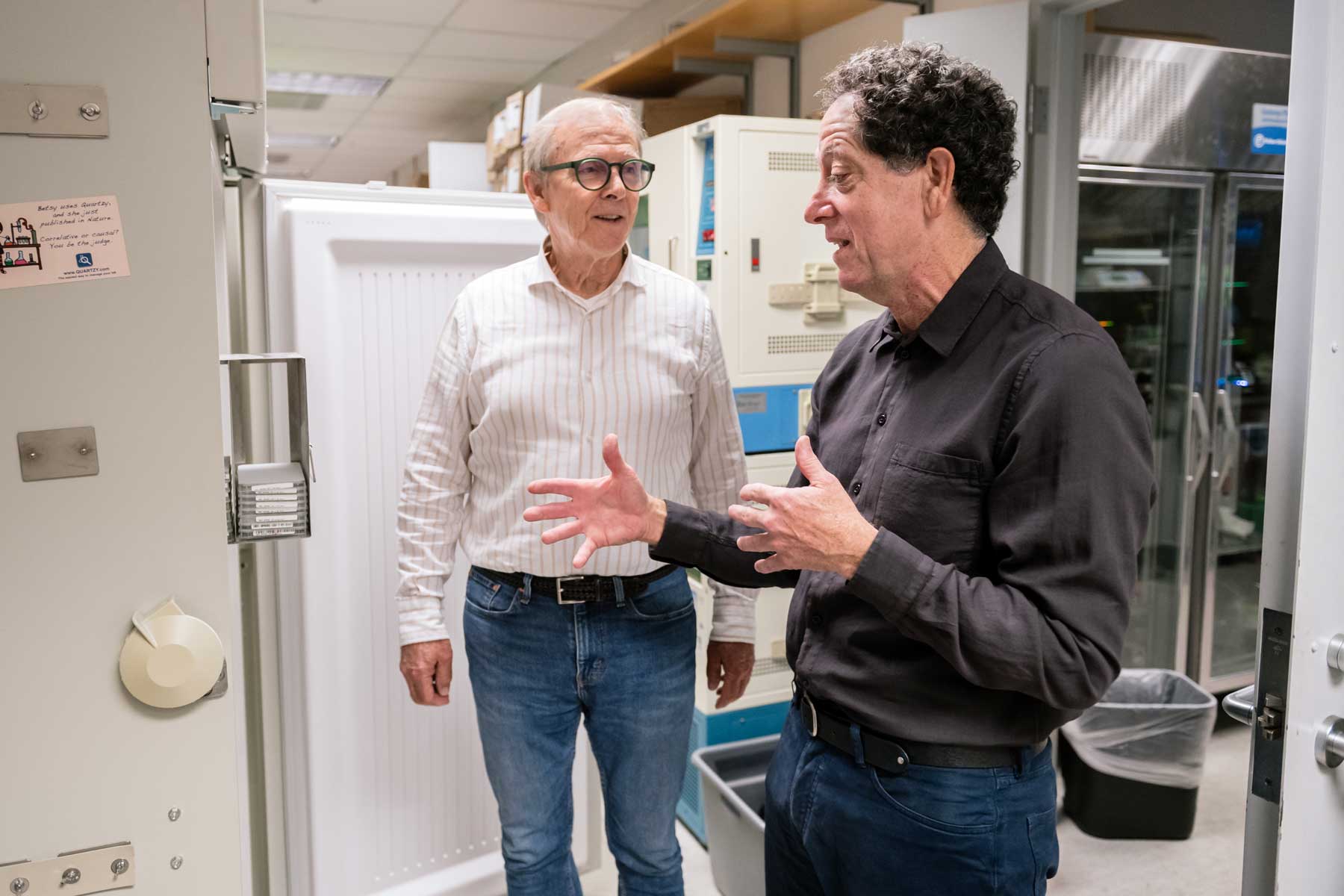 Kevan Shokat and Jim Wells engaged in discussion as they stand in front of a freezer in a lab.