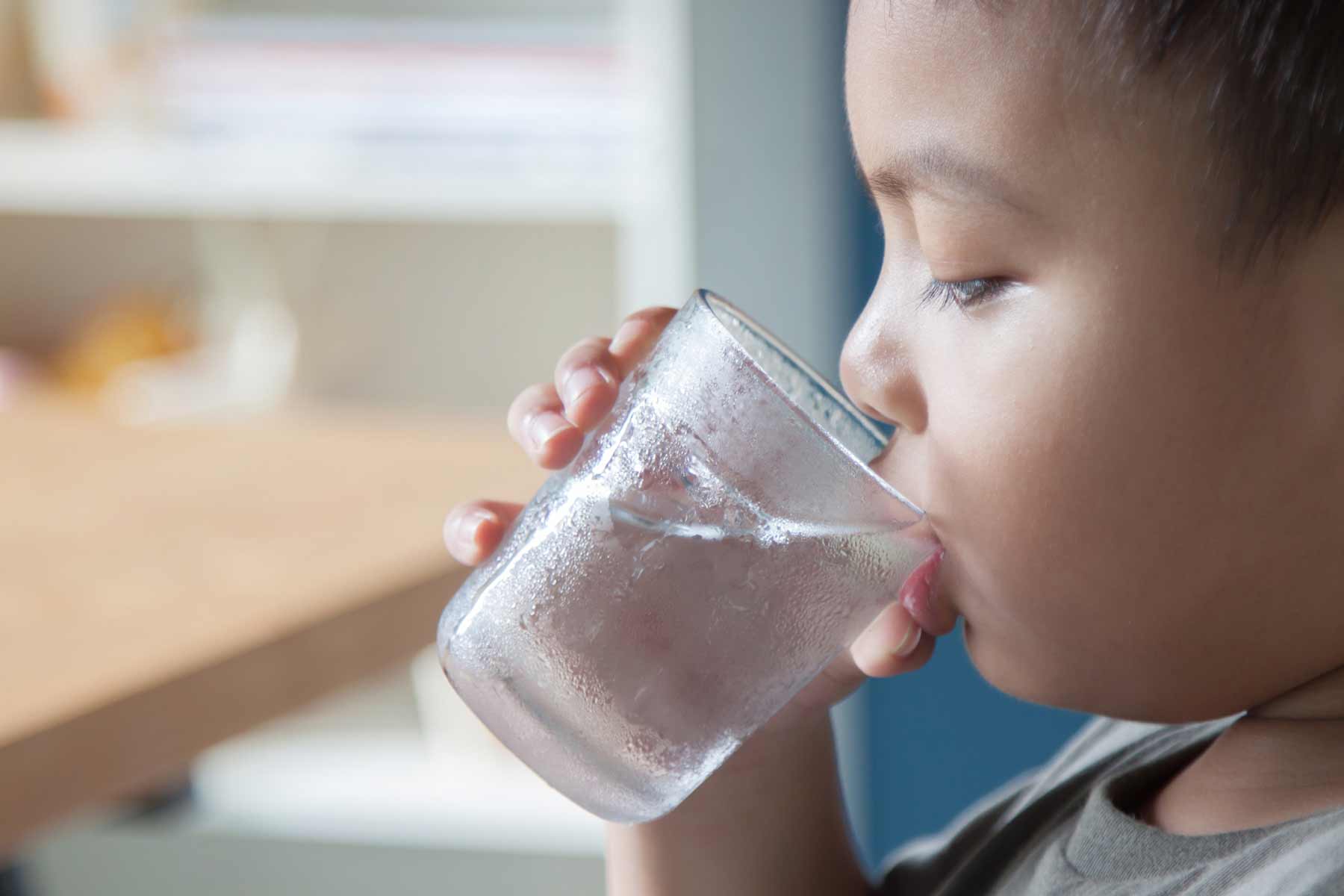 A young boy in toddler age drinks water from a glass.