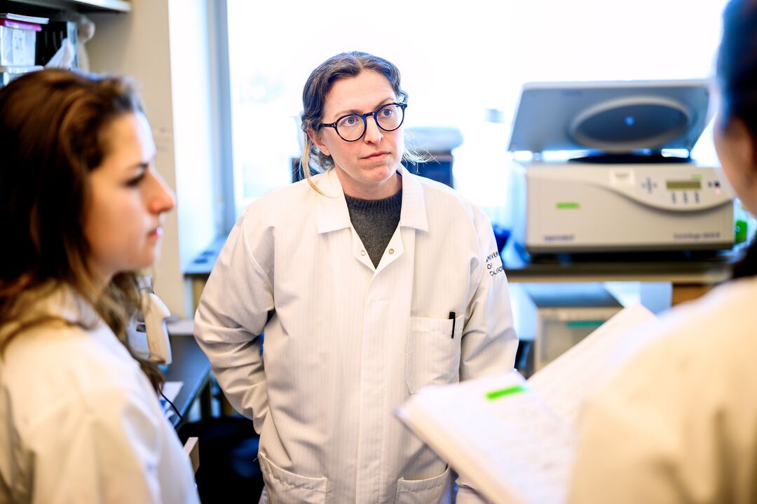 Three women wearing lab coats speak together in a lab.