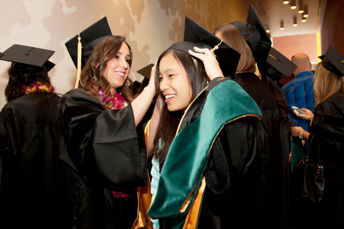 Physical Therapy student Lindsey Gendreau adjusts the cap for classmate Michelle Ho during their commencement ceremony.