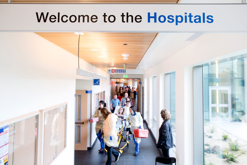Patient is on the hospital gurney, being transported to the room. On the top of the image is a sign  "Welcome to the Hospitals".