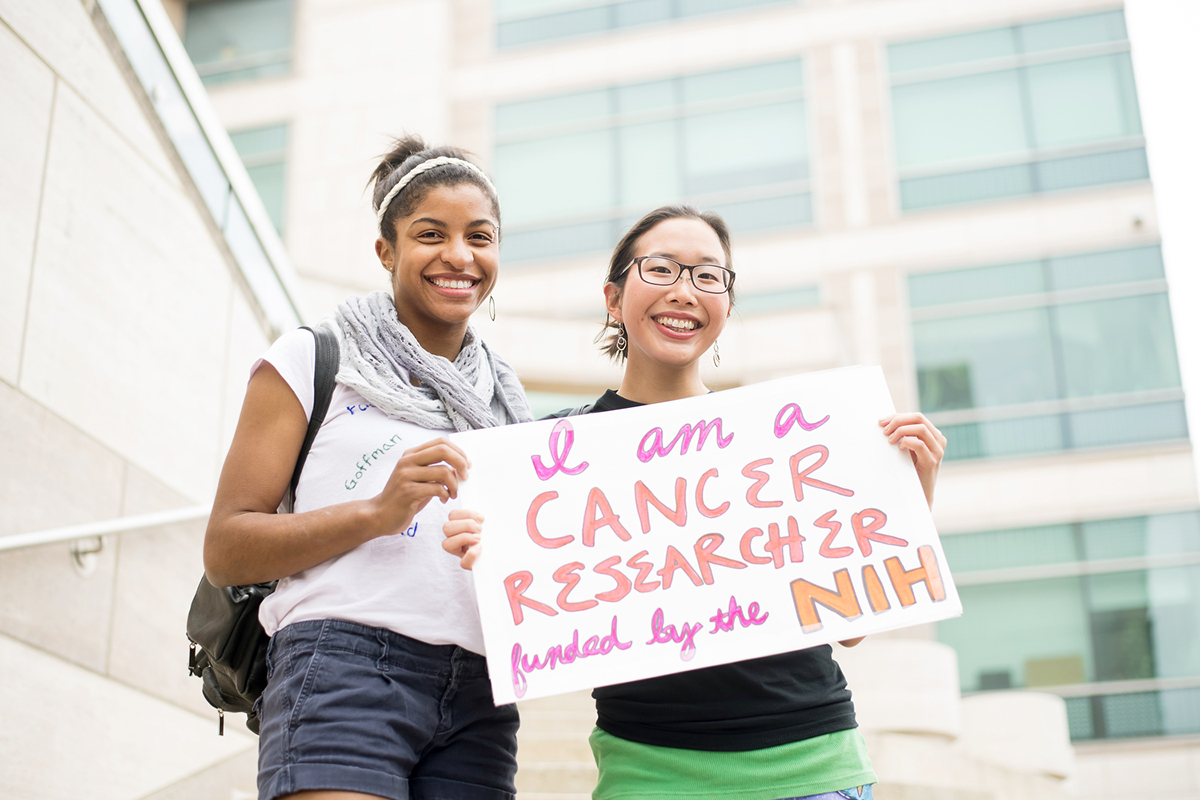 UCSF students Jhia Jackson (left) and Allison Wong hold a sign in support of federal funding for research during Stand Up for Science rally.