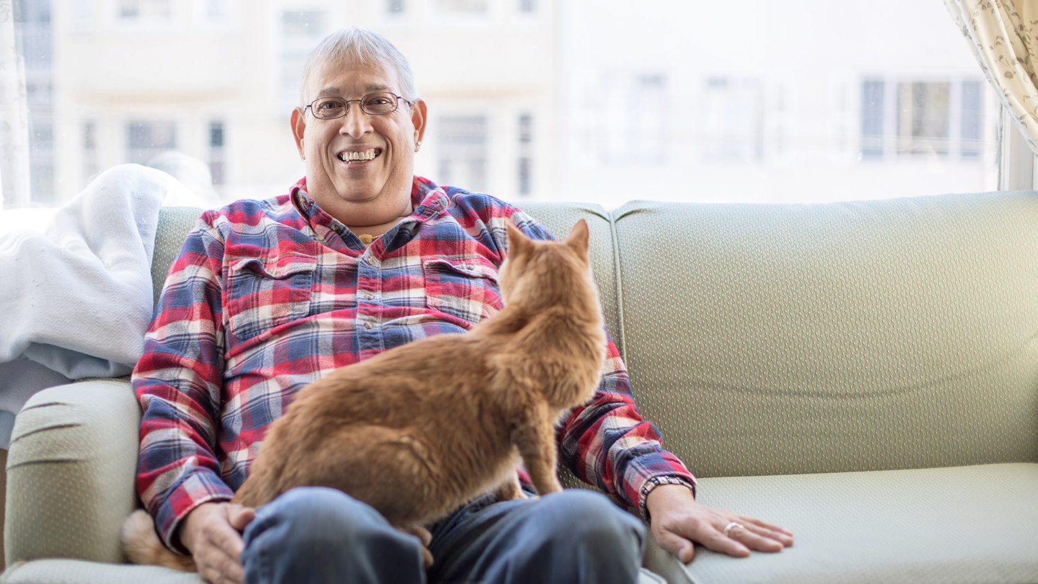 Reynaldo Garza sits on a couch with his cat
