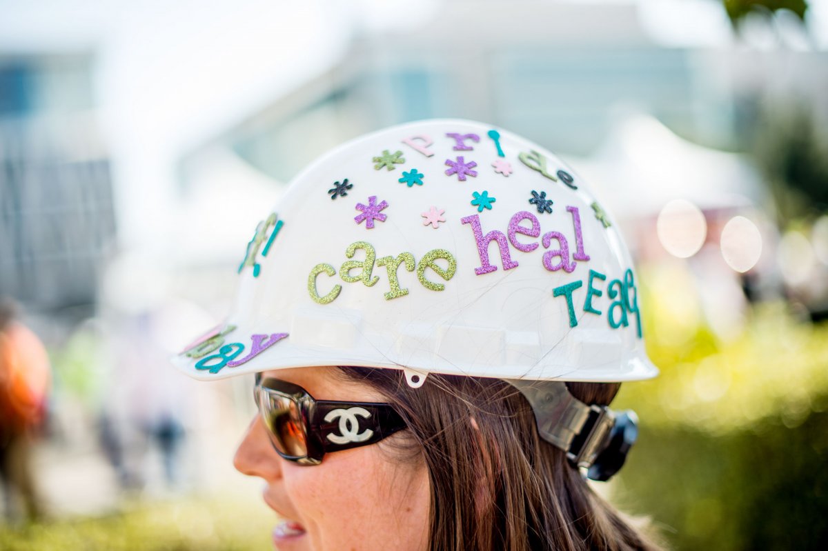 Sheena Fitzpatrick, a front desk supervisor at the UCSF Helen Diller Comprehensive Cancer Center, dons a white hard hat decorated with colorful glitter flowers and words "Pride", "Care", "Heal", "Team". 