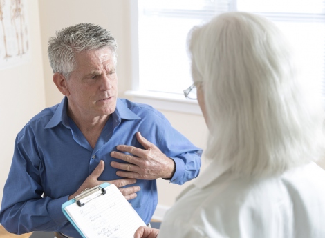 A stock image shows a man holding his chest while talking with a doctor