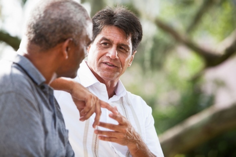 senior Latino man talks to a senior black man on a park bench