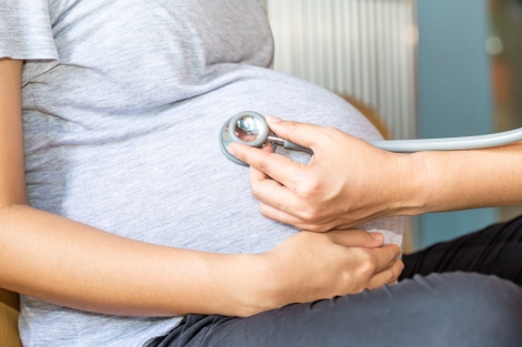 closeup of woman's pregnant belly with doctor holding a stethoscope to it