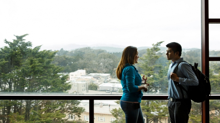 2 students talking in front of a picture window overlooking the Sunset district