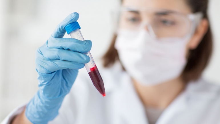 stock image of lab technician holding up a blood vial