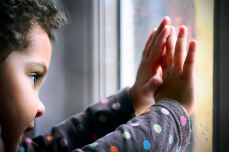 Child holding his hands against a window
