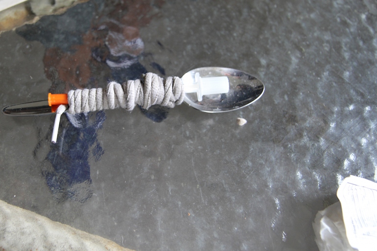 a needle tied to a spoon with a shoelace sitting on a table