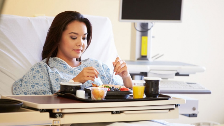 stock image of female patient eating a meal in her hospital bed