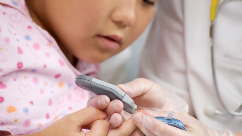 A child has a finger prick done by a health professional for a diabetes test.