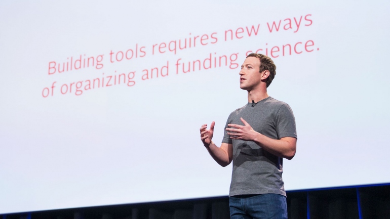 Mark Zuckerberg on stage in front of a slide that says "Building tools requires new ways of organizing and funding science."