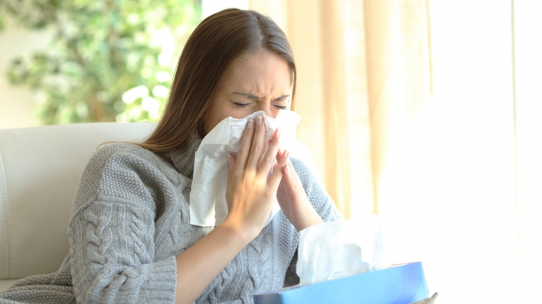a sick woman blows her nose into a tissue