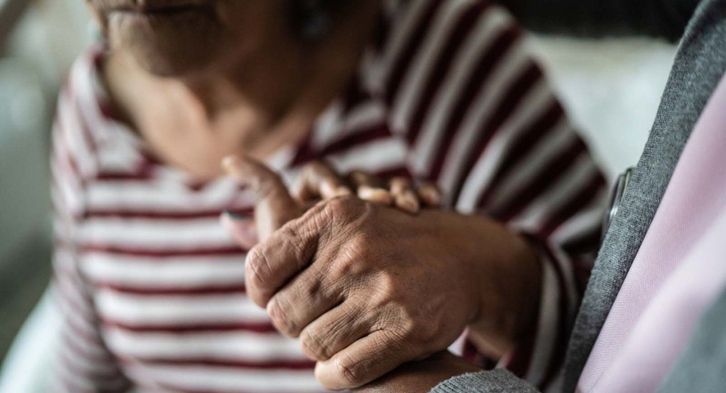 An elderly woman holds the hand of a caregiver while she gets up
