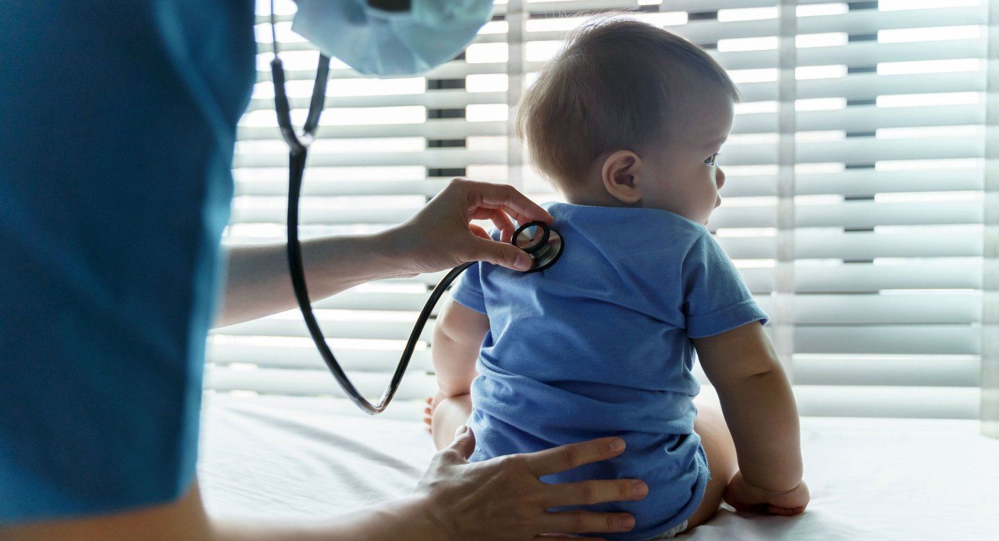 A health professional places a stethoscope to a baby's back