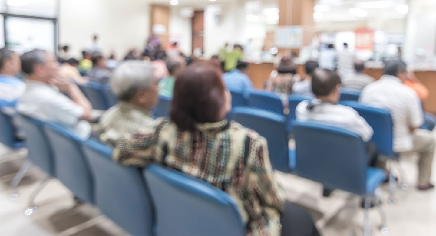 Patients sit in chairs in a crowded emergency waiting room.