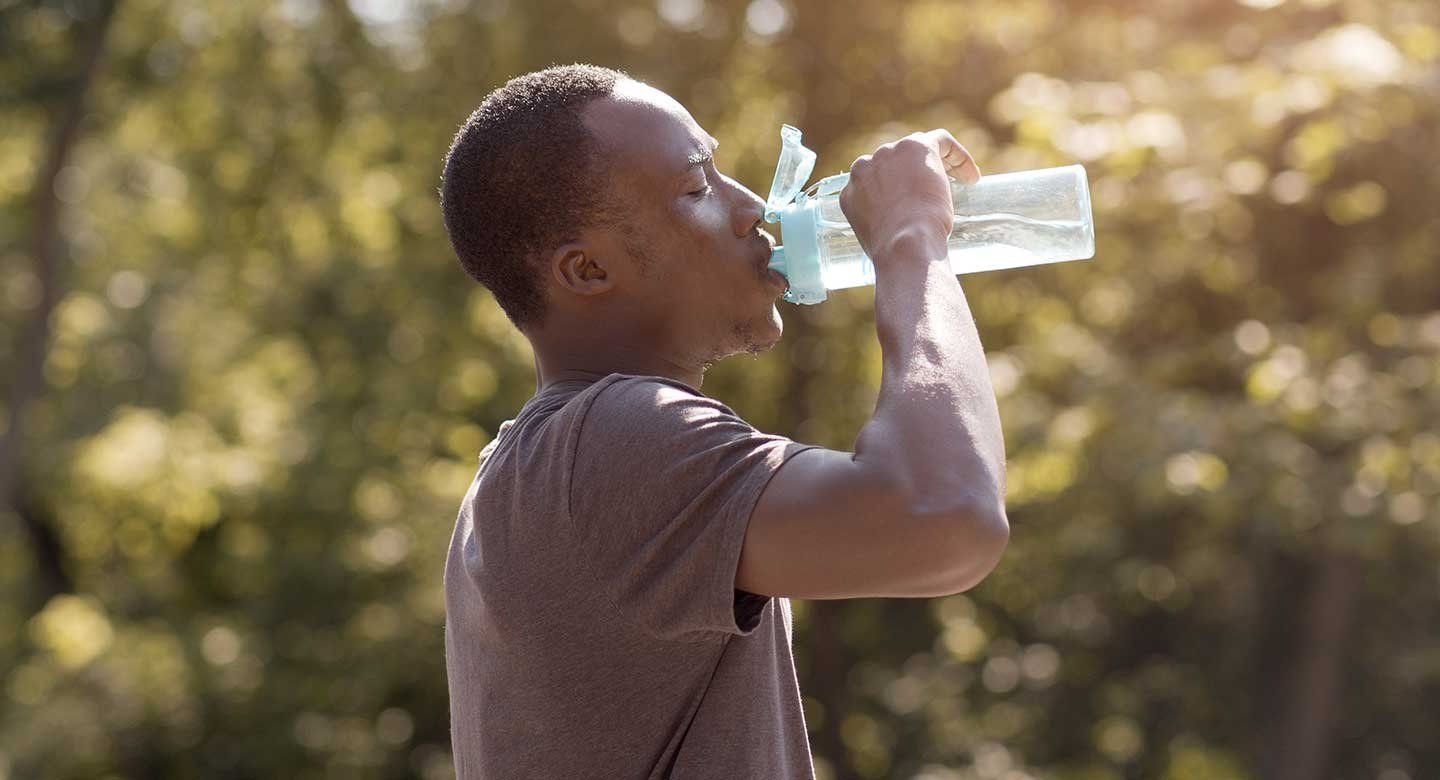 A black man drinks water otuside on a hot day.