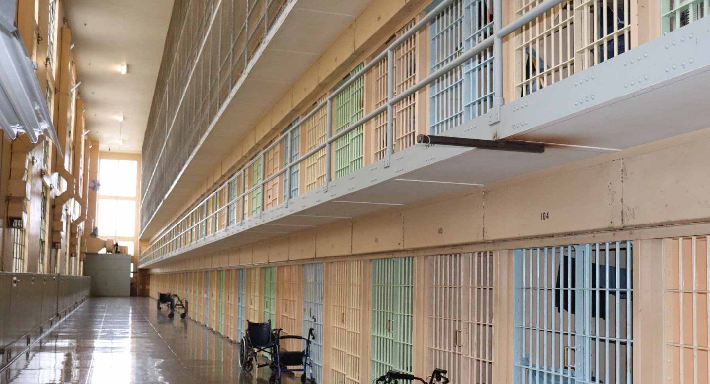 Interior of the Oregon State Penitentiary’s E-block housing unit. Multiple floors have barred units, and there are wheelchairs and walkers outside some of the units.