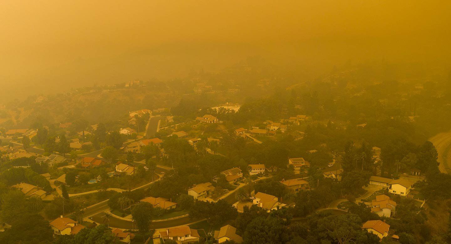 A haze of yellow smoke hangs over homes in a hilly residential neighborhood in California.