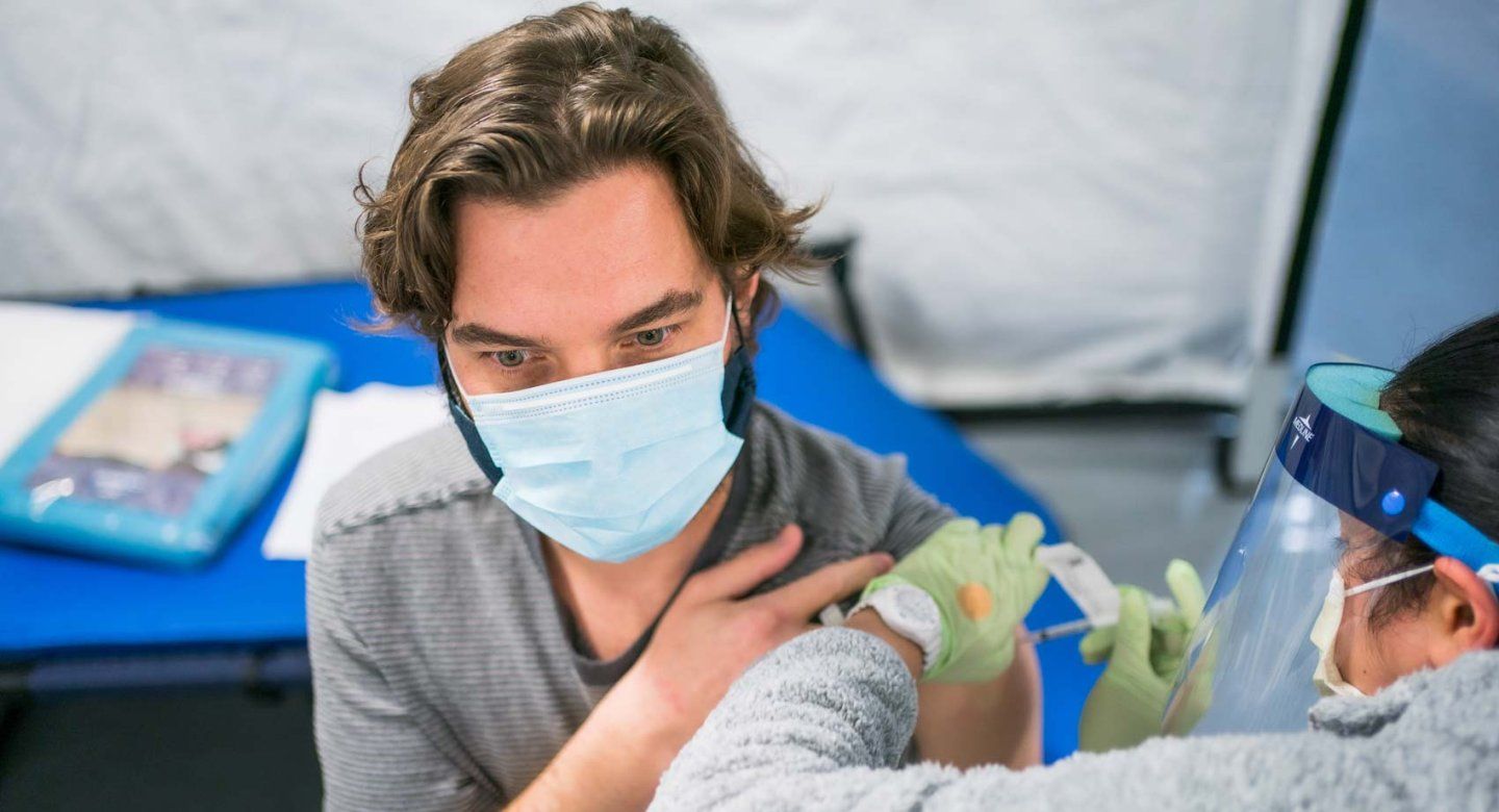 A medical professional gives a vaccine to a man wearing a surgical mask.
