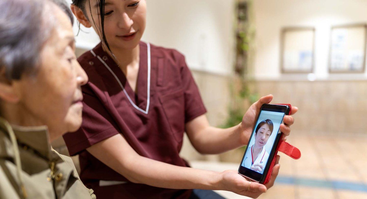 A younger woman holds out a phone so that an elderly woman can see her doctor.